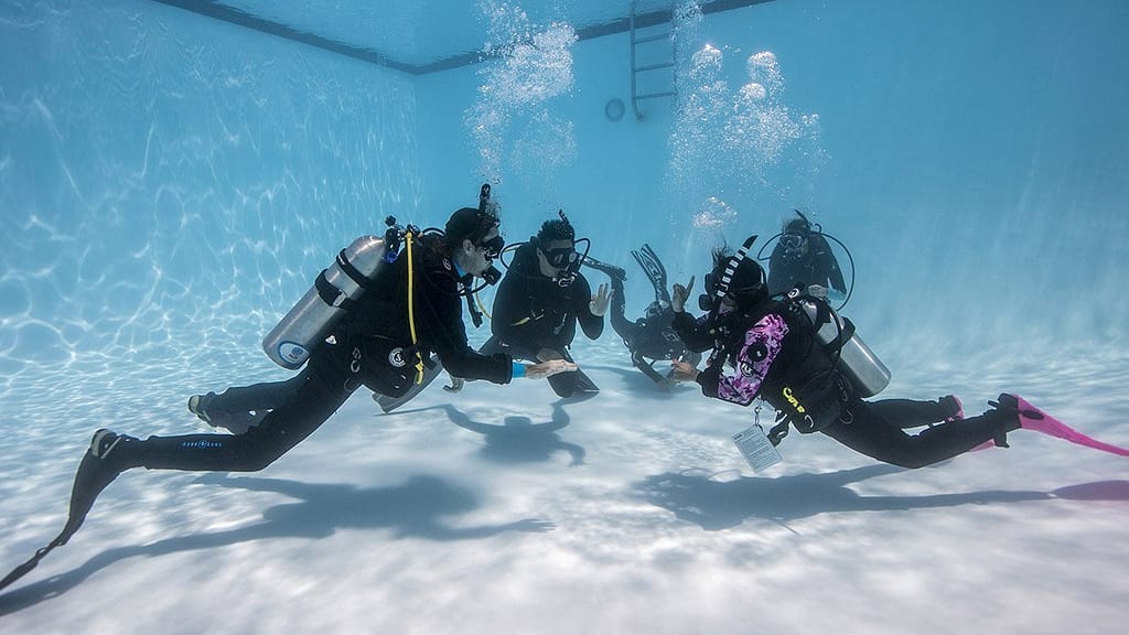 four scuba divers underwater in a pool