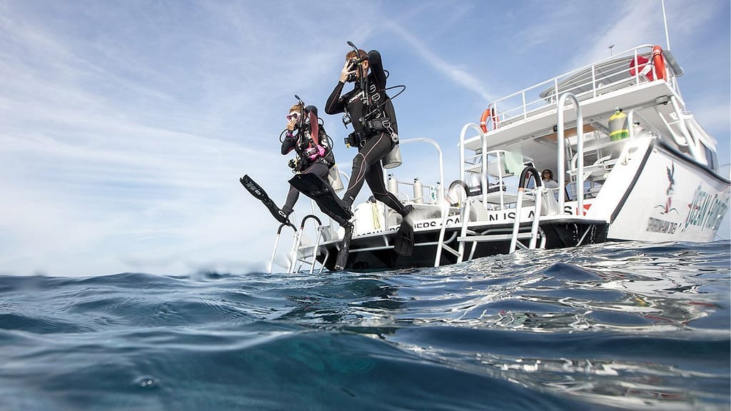 two scuba divers jumping from the boat into water